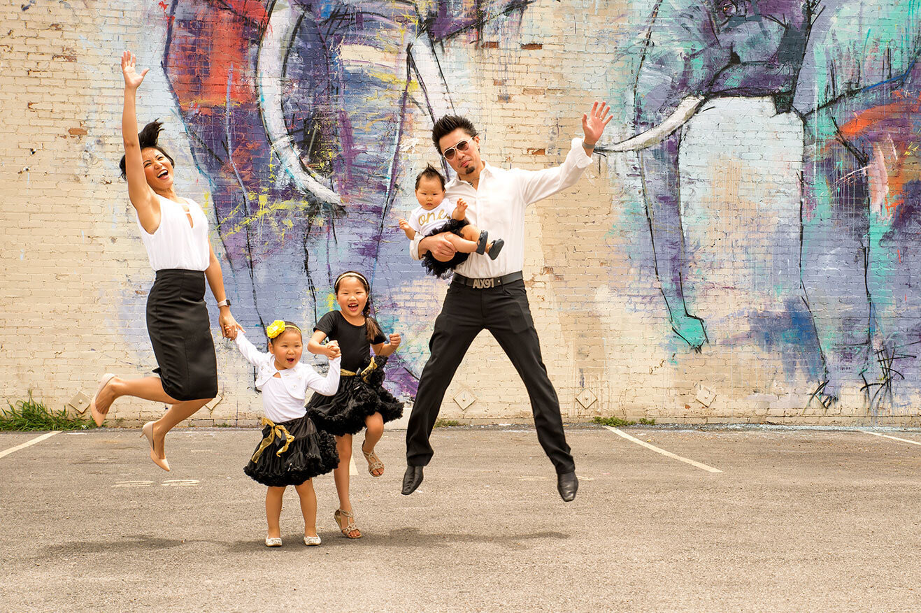 A family of five jumping and laughing in front of a colorful elephant mural in Deep Ellum