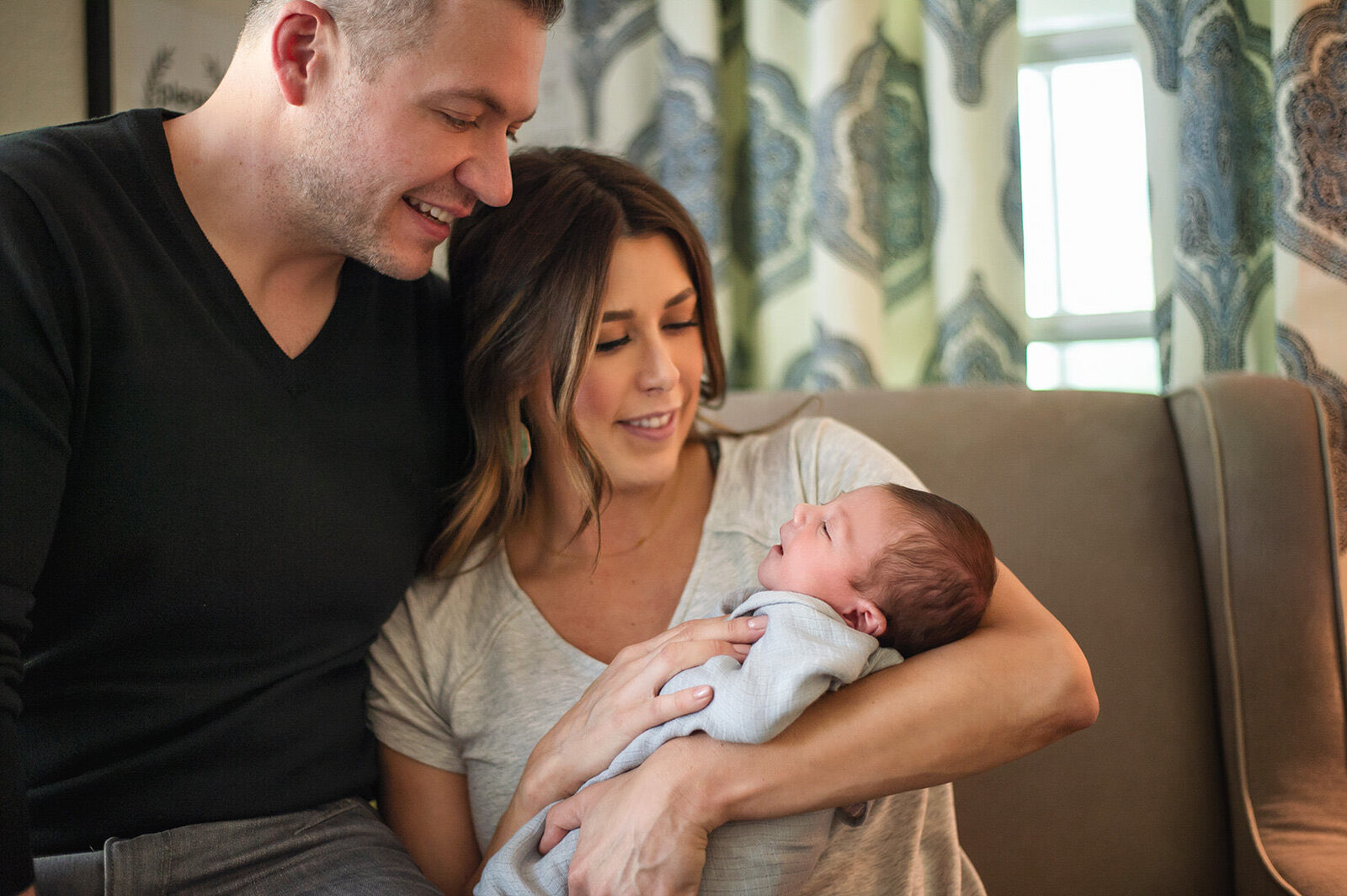 New parents smiling down at their newborn on the living room couch during an in-home session