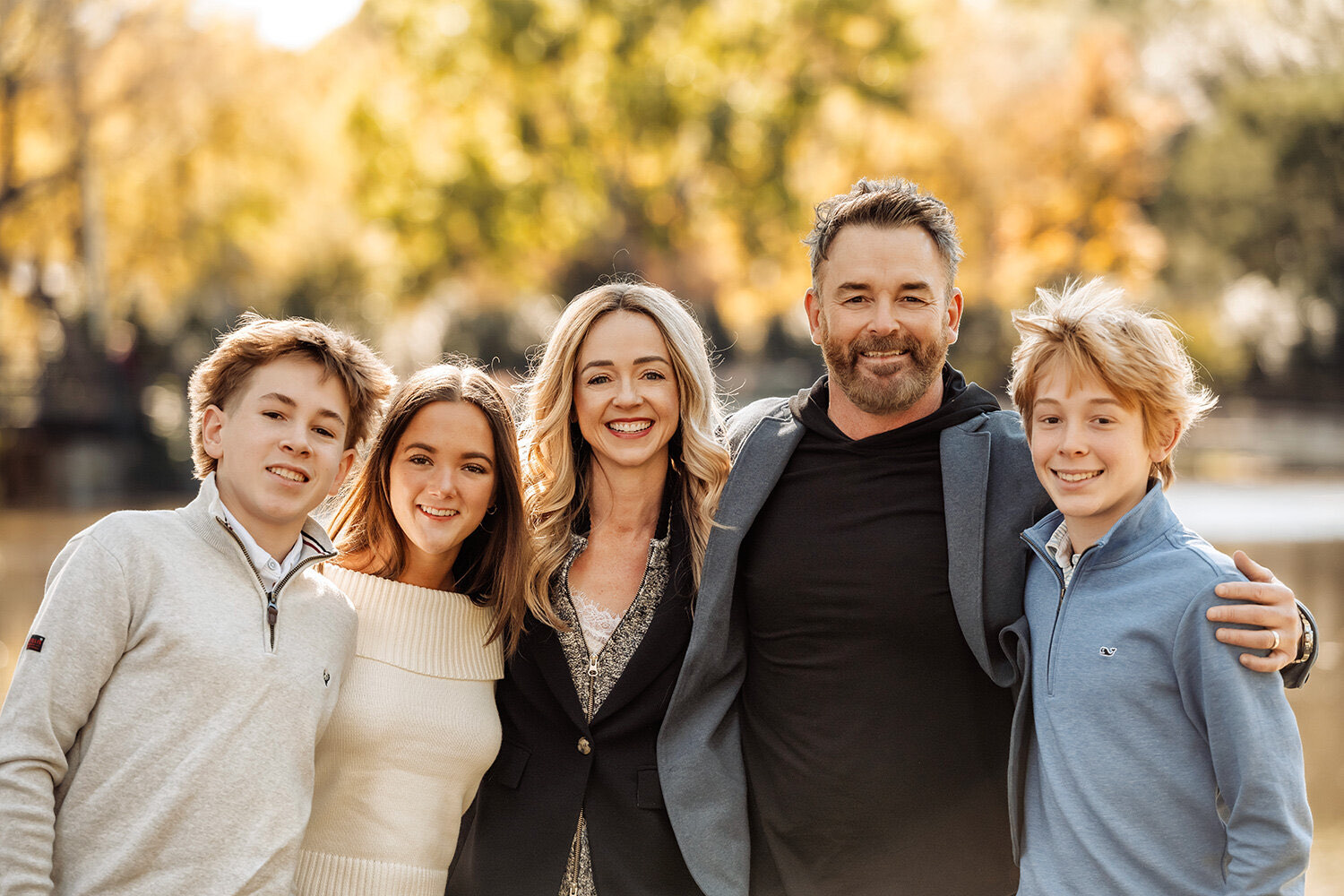 A family of five smiling together in warm autumn light at Lakeside Park
