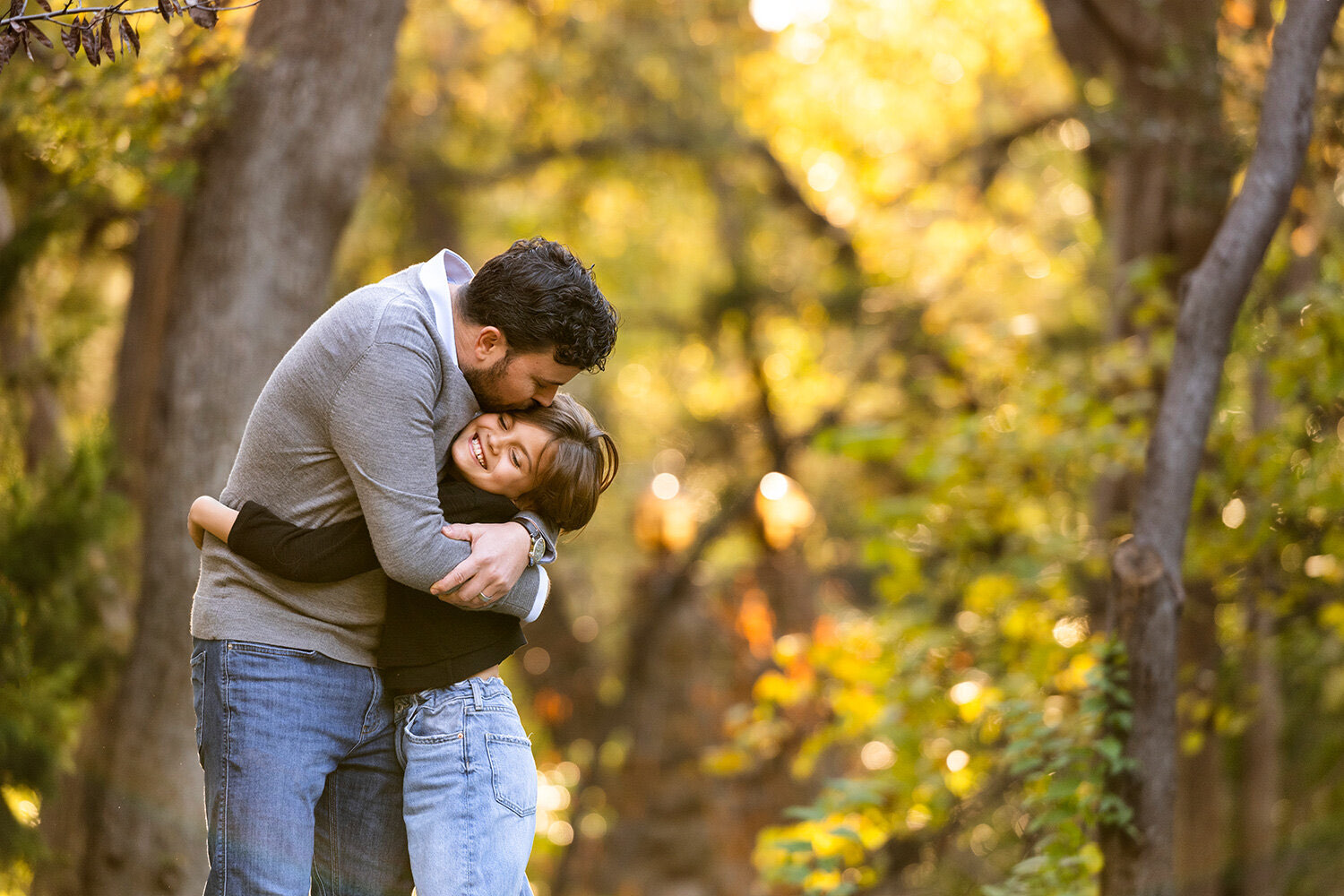 A father kissing his laughing daughter on the head in golden light at Prather Park